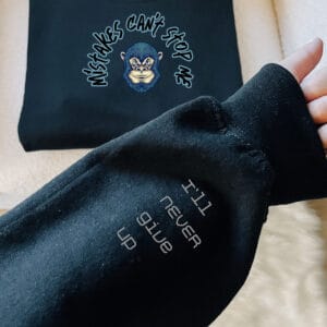 Navy blue hoodie displaying "Mistakes Can't Stop Me" arched-lettering across the chest and "I'll never give up" printed on the sleeve.