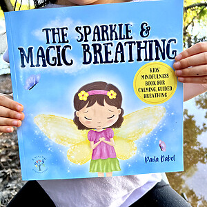 female child holding book "The Sparkle & Magic Breathing", an emotional intelligence book for kids.