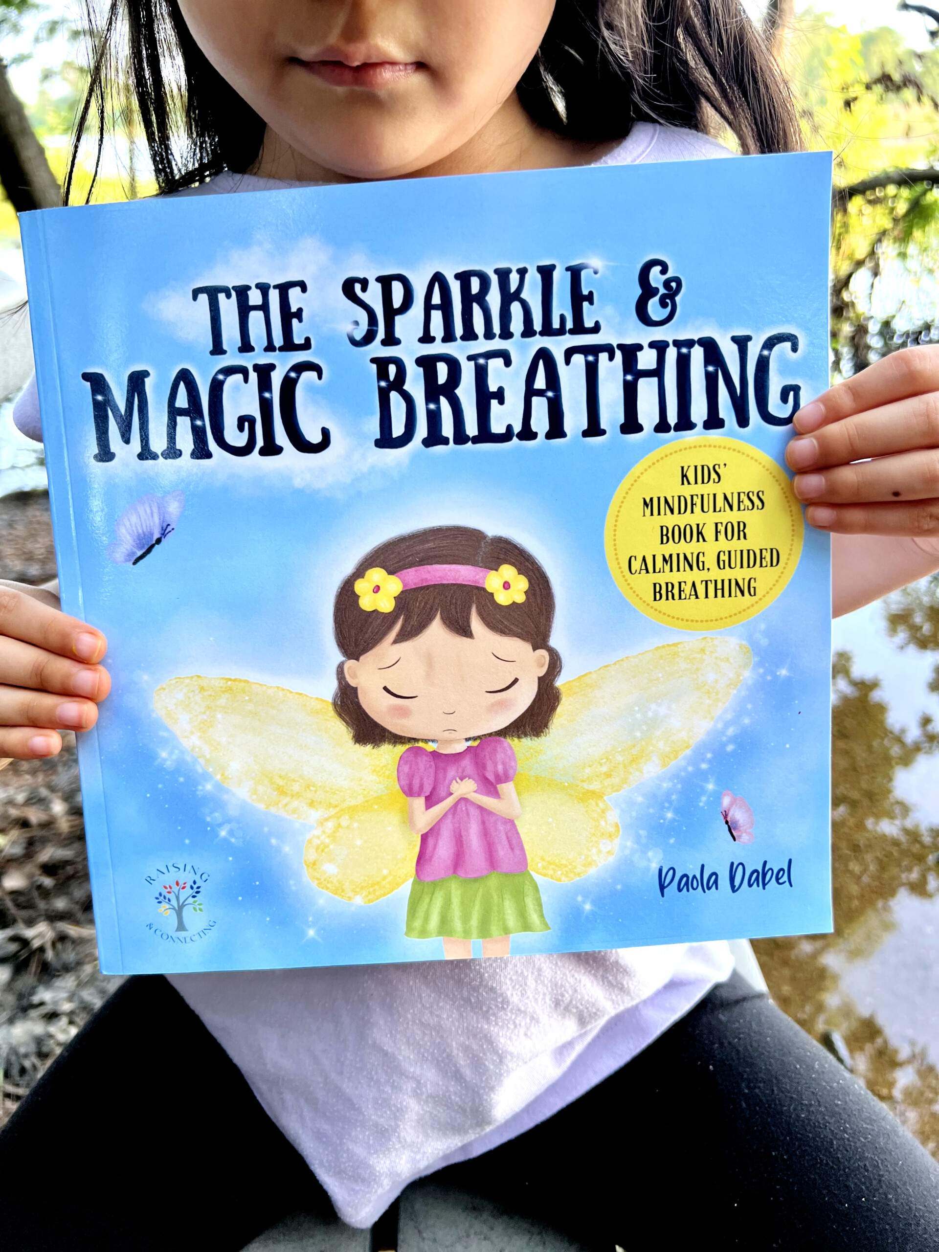 female child holding book "The Sparkle & Magic Breathing", an emotional intelligence book for kids.